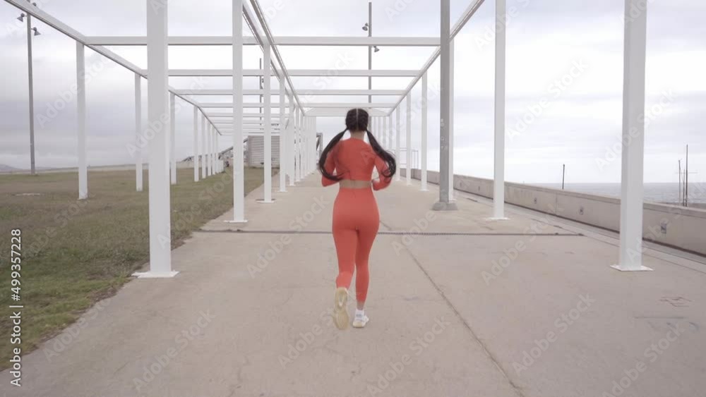 Back view of a beautiful caucasian woman athlete running on city street training intense endurance workout focused female sport urban morning sunrise slow motion Back view of a beautiful caucasian woman athlete running on city street training intense endurance workout focused female sport urban morning sunrise slow motion