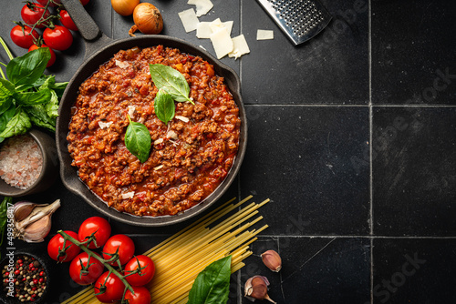 classic italian bolognese sauce stewed in a pan with ingredients on black tile background, top view photo