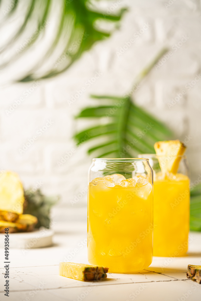 Pineapple cocktail or juice in two glasses with ice on white background with palm leaves Pineapple cocktail or juice in two glasses with ice on white background with palm leaves