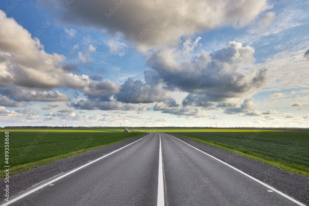 Empty asphalt highway outside the city among green fields and against a beautiful cloudy sky