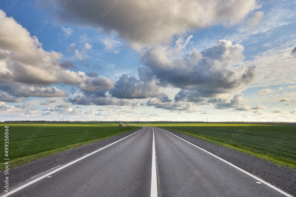 Empty asphalt highway outside the city among green fields and against a beautiful cloudy sky Empty asphalt highway outside the city among green fields and against a beautiful cloudy sky