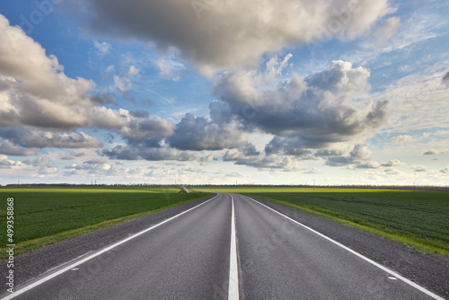 Empty asphalt highway outside the city among green fields and against a beautiful cloudy sky