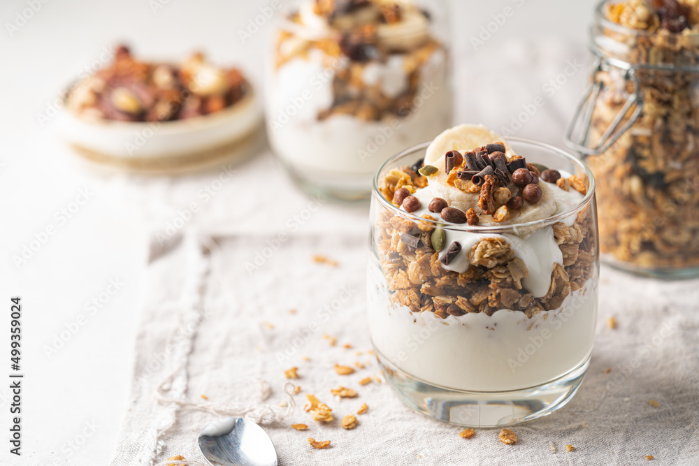 Crunchy granola with yogurt, banana, nuts, chocolate and honey in a glass on white background. Healthy breakfast concept. Crunchy granola with yogurt, banana, nuts, chocolate and honey in a glass on white background. Healthy breakfast concept.