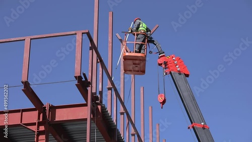 Male builders work at height in a lifting cradle, creating the iron frame of the building.