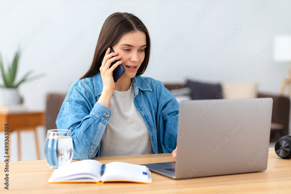 Young Caucasian woman freelancer or office employee working remotely using laptop and talking on a mobile phone at home office or coworking sitting at workplace Young Caucasian woman freelancer or office employee working remotely using laptop and talking on a mobile phone at home office or coworking sitting at workplace
