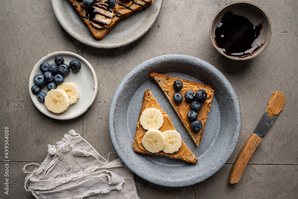 Peanut butter toast with banana slices and chocolate. Healthy breakfast or snack on grey concrete background., top view