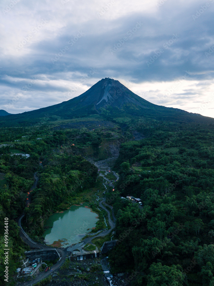 The view of Mount Merapi with the Bebeng River and a lake that holds water, the sky looks cloudy. Forest vegetation that looks still dense with trees surrounding the lake. Bego Pendem, Mount Merapi