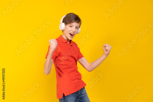 Relaxed young man in casual red shirt posing isolated on yellow background, studio portrait. People lifestyle concept. Layout copy space. Listen to music with headphones, dancing, raising hands