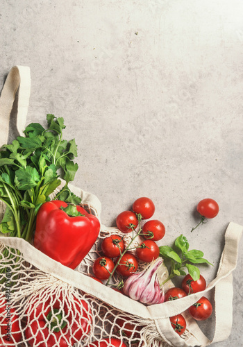 Food background with various vegetables and herbs in reusable shopping bag at pale beige concrete kitchen table.Coriander, red bell pepper, tomatoes and basil leaves.Sustainable plastic free. Top view