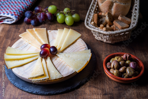 Spanish cheese board accompanied by grapes, olives and assorted bread.