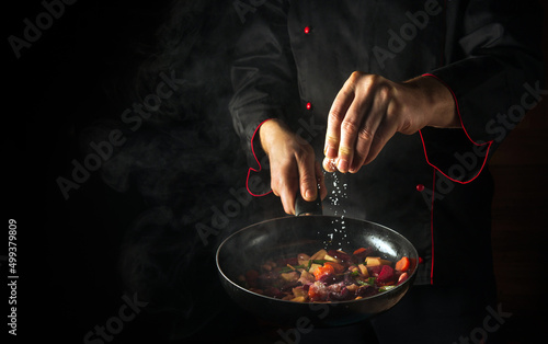 Fototapeta Naklejka Na Ścianę i Meble -  Cooking fresh vegetables. The chef adds salt to a steaming hot pan. The idea of European cuisine for a hotel with advertising space.