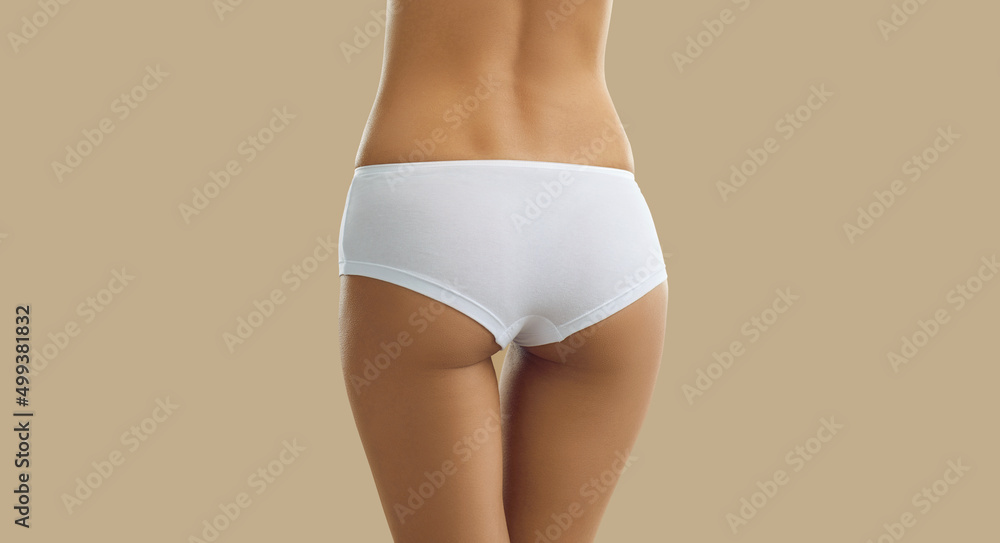 Perfect female body. Slender woman with beautiful buttocks posing in white  panties on beige background. Cropped image close up rear view on woman's  buttocks in white comfortable cotton panties. Banner Photos