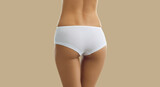 Perfect female body. Slender woman with beautiful buttocks posing in white panties on beige background. Cropped image close up rear view on woman's buttocks in white comfortable cotton panties. Banner