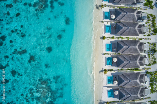 Aerial top view of pool villas, bungalows in Maldives paradise tropical beach. Amazing blue turquoise sea lagoon, ocean bay water. Luxury travel vacation destination. Beautiful sunny aerial landscape