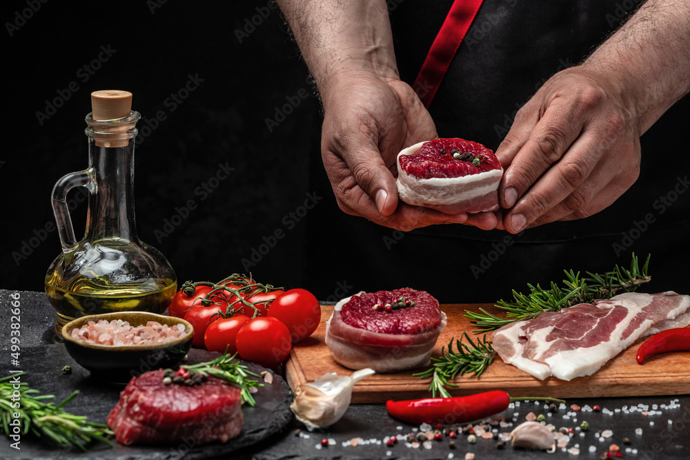 chef hands cooking Beef medallions wrapped in bacon with rosemary and spices on black background. Restaurant menu, dieting, cookbook recipe. place for text