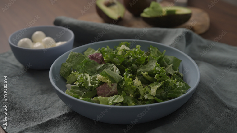 Man making salad with mixed greens avocado and mozzarella in blue bowl Man making salad with mixed greens avocado and mozzarella in blue bowl