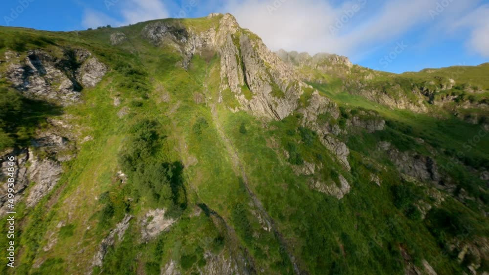 Aerial fpv view raising up mountain ridge rocky texture to summit covered green grass smoke blue sky. Shooting from drone dive to narrow gorge cliff structure organic wild nature environment scenery Aerial fpv view raising up mountain ridge rocky texture to summit covered green grass smoke blue sky. Shooting from drone dive to narrow gorge cliff structure organic wild nature environment scenery