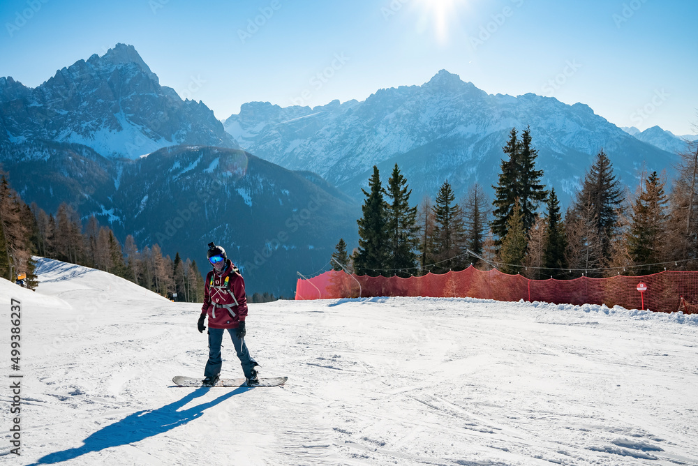 Snowboarder standing on snowy mountain slope at winter resort on sunny day