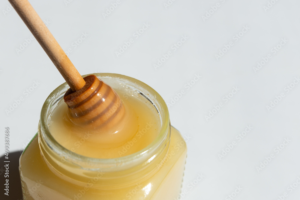 yellow honey with a wooden spoon in a transparent glass jar on a white background close up..cotton honey yellow honey with a wooden spoon in a transparent glass jar on a white background close up..cotton honey