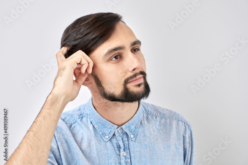 Smart brunette man in casual touches head thinks doubts, makes decision isolated on blue studio background
