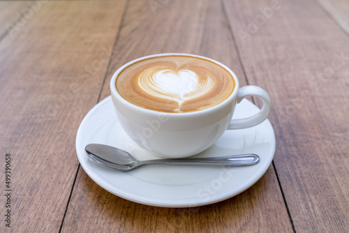 Latte coffee or cappuccino coffee in white cup with beautiful heart shape latte art on wooden table.