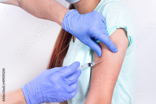 Female doctor or nurse giving shot or vaccine to patient s shoulder - young girl. Close-up. Vaccination against flu  pandemic coronavirus. Mandatory prevention of people for immunity from the virus.