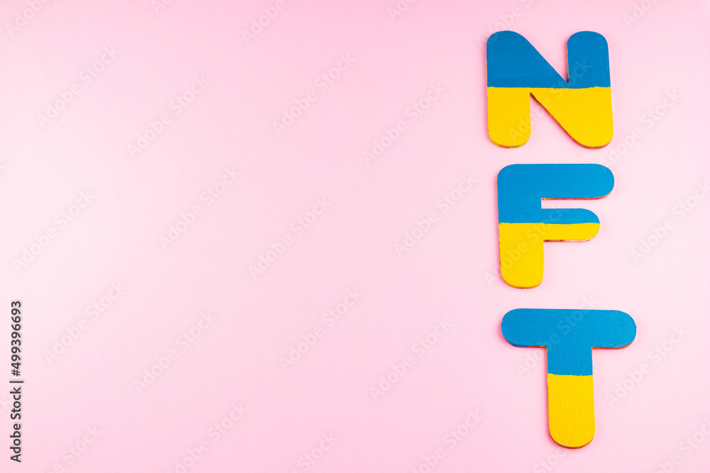NFT Non-Fungible Token in Ukrainian flag colors. Blue-yellow NFT inscription on pink background. Ukraine support concept. Top view. Copy space