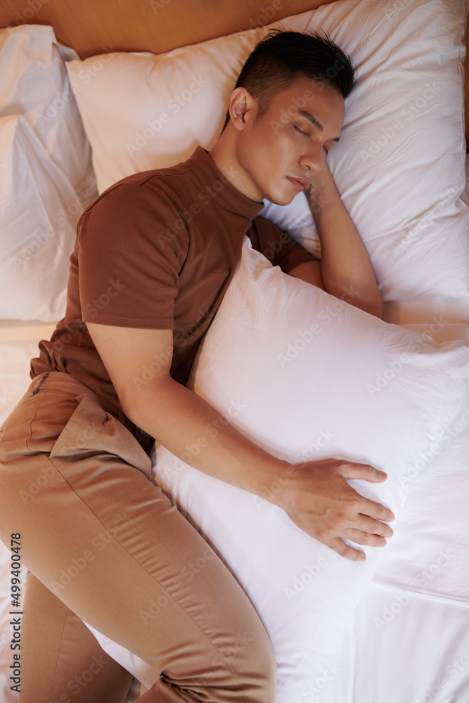 Young man sleeping with pillow between legs, which keeps his pelvis neutral  and prevents spine from rotating during night Stock Photo