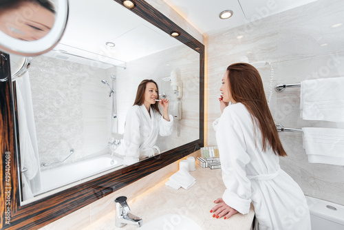 A young beautiful girl is brushing her teeth in a beautiful white bathroom. A fresh good morning at the hotel. Rest and travel. Hotel recreation, and tourism.