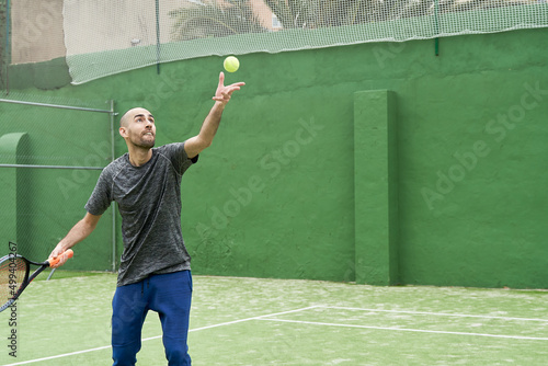 Foto Amateur tennis player learns to serve at court with ball and racket