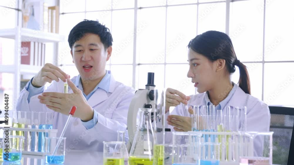 Team of young Asian female and male colleague scientists using microscope and holding a test tube in life science research laboratory - 4k Quality Footage Team of young Asian female and male colleague scientists using microscope and holding a test tube in life science research laboratory - 4k Quality Footage