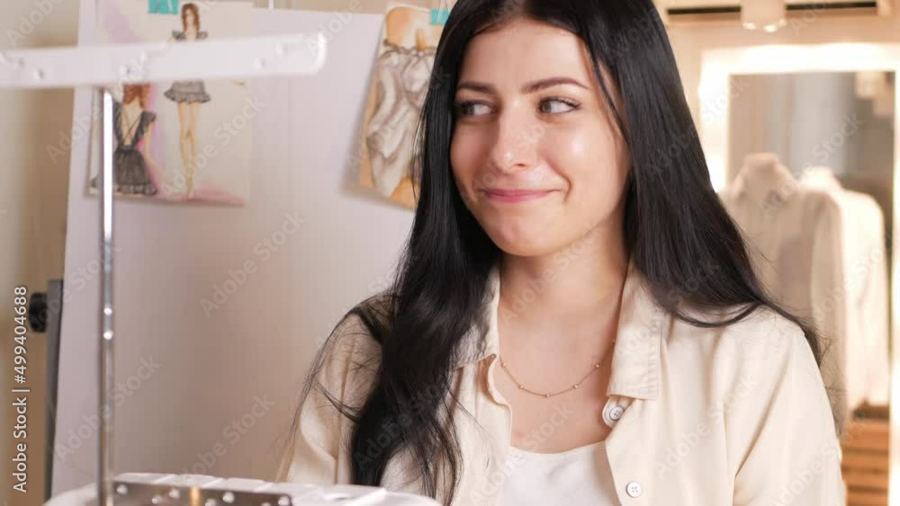 black haired seamstress in atelier, portrait at work. Table with fabric and sewing tools, indoors. Funny black haired seamstress in atelier, portrait at work. Table with fabric and sewing tools, indoors. Funny