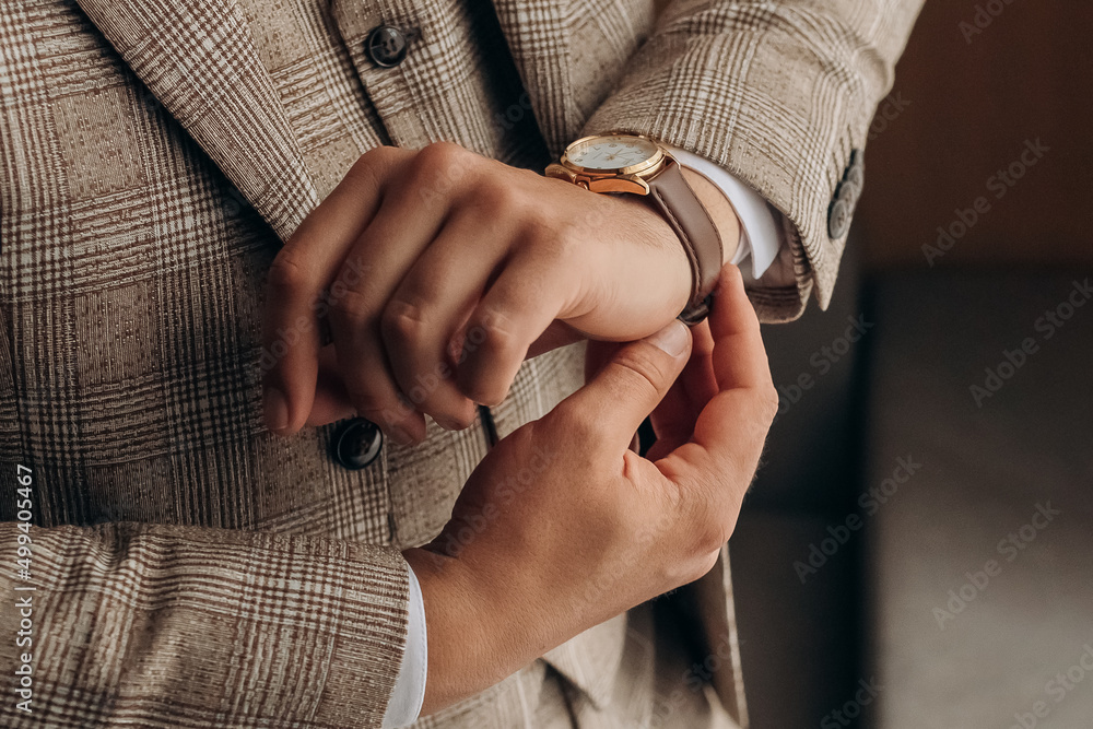 Close photo of details of man's clothes. Morning of the groom. Stylish guy in a suit fastens a watch on his hand, standing by the window. Close photo of details of man's clothes. Morning of the groom. Stylish guy in a suit fastens a watch on his hand, standing by the window.