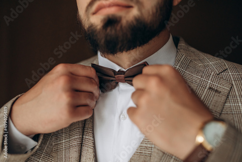 Fotobehang A man with a beard in a stylish suit with a watch on his arm fixes a bow tie