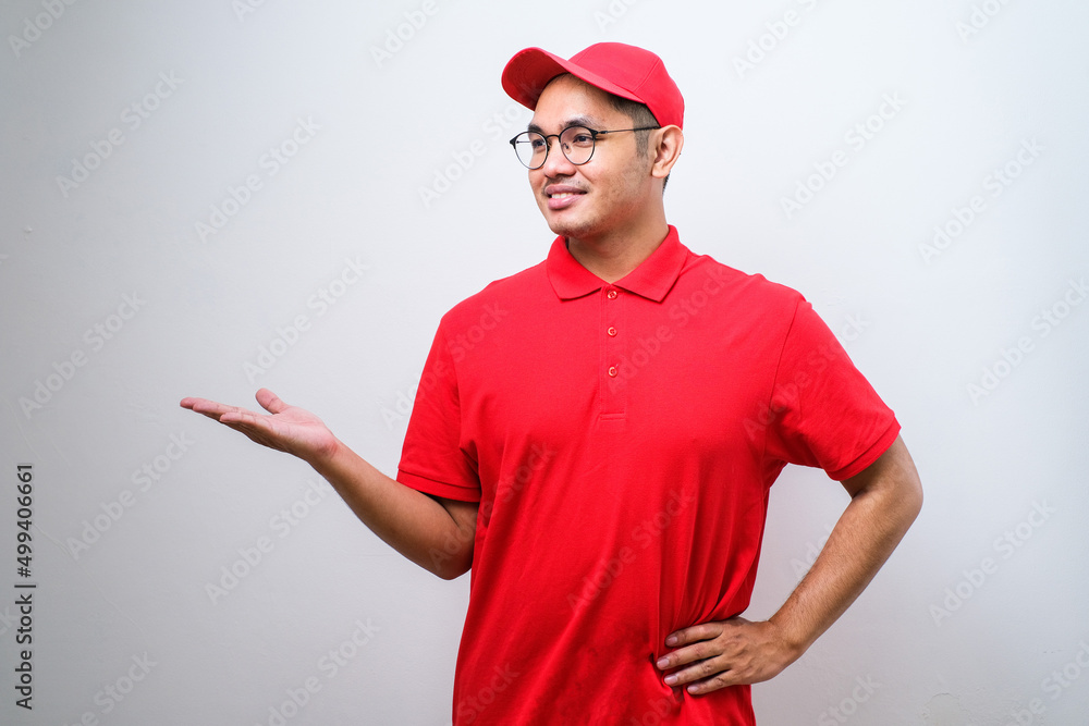 Young handsome chinese delivery man pointing with hand and finger to the side looking at the camera. Young handsome chinese delivery man pointing with hand and finger to the side looking at the camera.