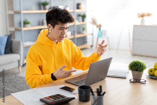 Asian guy using laptop wearing earphones sitting at desk