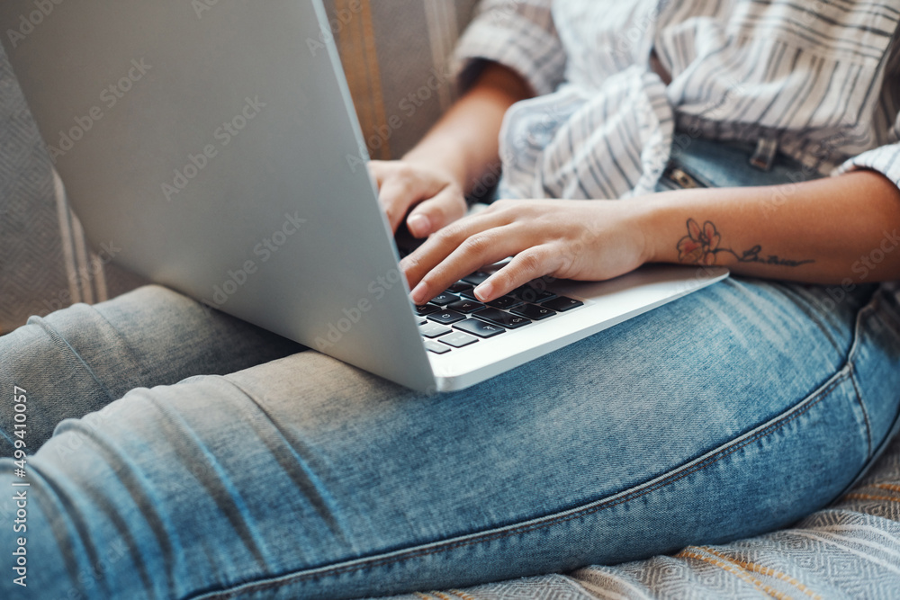 Working on her blog. Cropped shot of an unrecognizable woman using her laptop while relaxing on a sofa at home. Working on her blog. Cropped shot of an unrecognizable woman using her laptop while relaxing on a sofa at home.