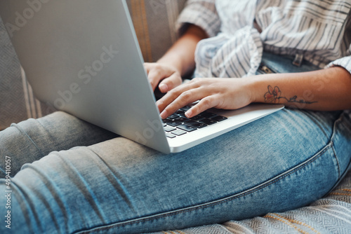 Working on her blog. Cropped shot of an unrecognizable woman using her laptop while relaxing on a sofa at home.