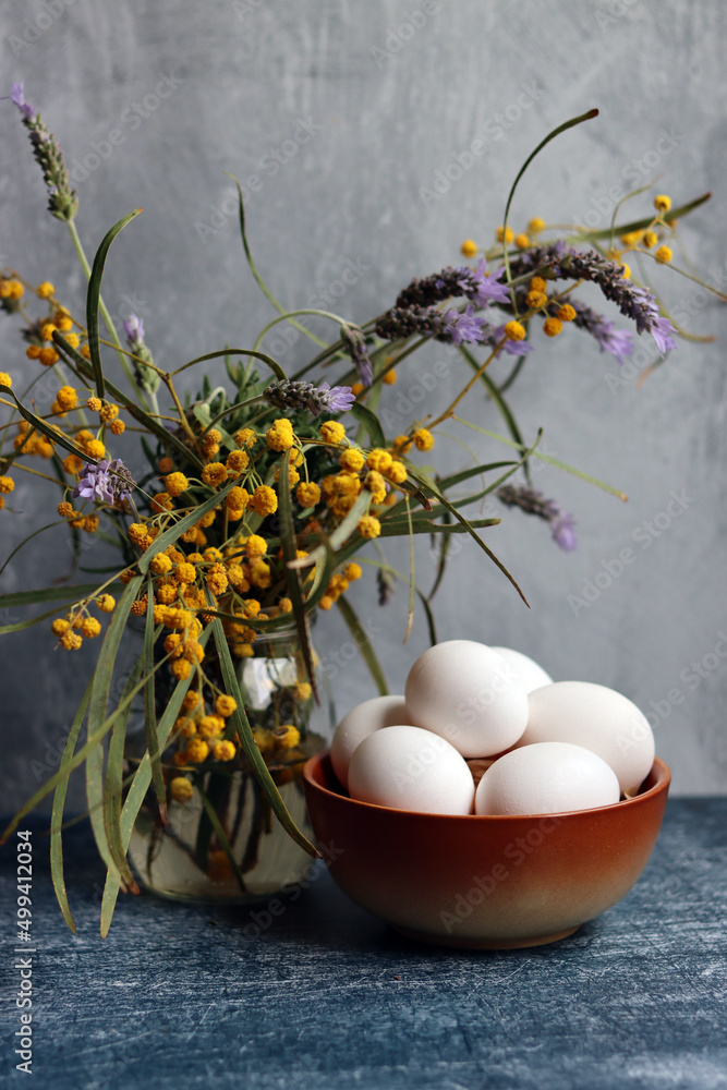 Still life with wild spring flowers in a vase. Beautiful yellow blossom of acacia. Grey textured background. 