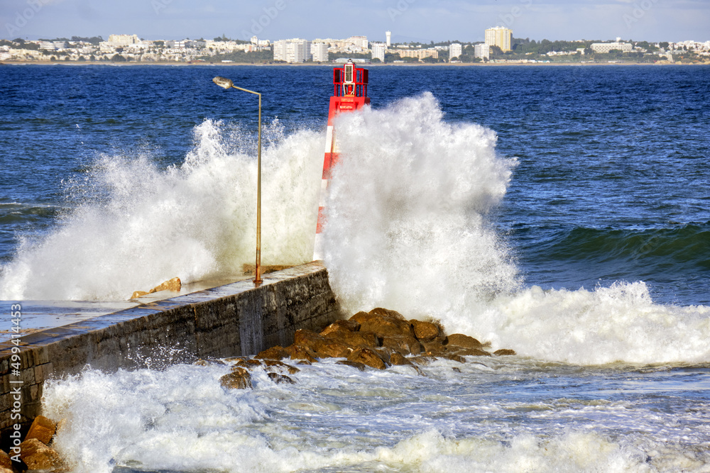 huge wave crashing over Lagos lighthouse and pier, Algarve, Portugal