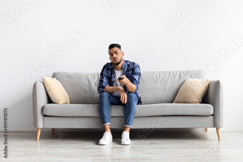 Bored young man watching television sitting on couch © Prostock-studio
