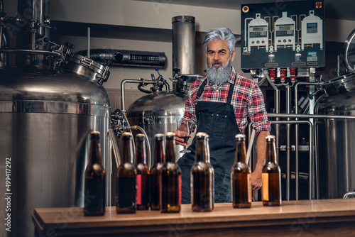 Production of quality beer. Old man brewer near table with beer looking at camera. © Fxquadro