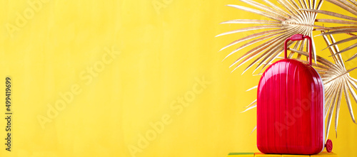Web banner with red suitcase and golden palm leaves against the yellow background. Travel and summer vacations concept. Mockup with copy space