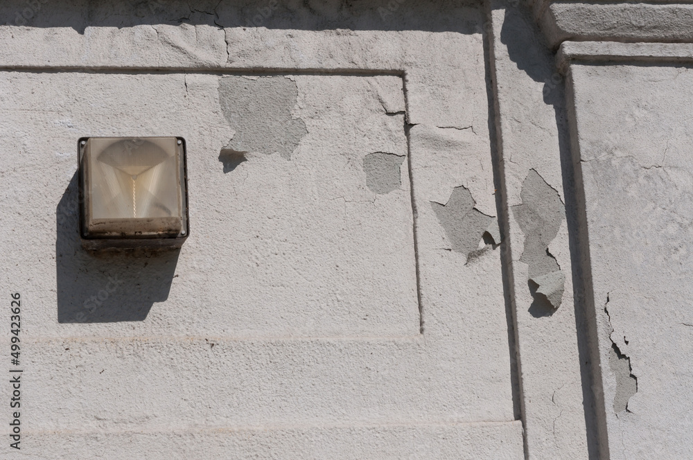 wall with peeling paint and security lamp in the sun