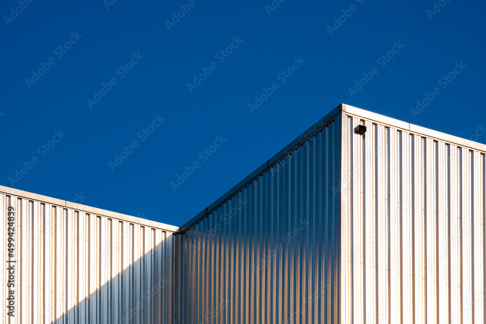 Sunlight reflection on surface of corrugated steel wall of industrial building against blue clear sky background in low angle view Sunlight reflection on surface of corrugated steel wall of industrial building against blue clear sky background in low angle view