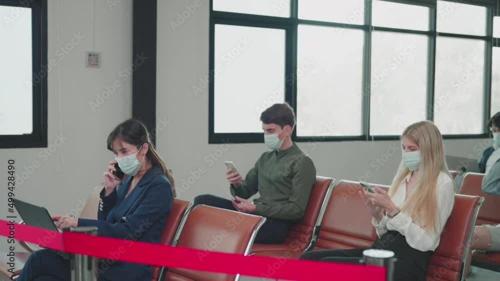 Airline passengers wear face masks sitting using smartphone and laptop while waiting for check-in at the airport. social distancing, New normal, Illness Prevention, Covid-19 concept Airline passengers wear face masks sitting using smartphone and laptop while waiting for check-in at the airport. social distancing, New normal, Illness Prevention, Covid-19 concept