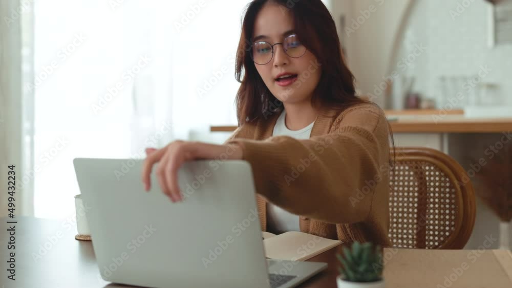 Dolly out of confident and cheerful asian woman opening and typing on a laptop. Young female professional writing an important email from her home. Modern living room. Remote working. Dolly out of confident and cheerful asian woman opening and typing on a laptop. Young female professional writing an important email from her home. Modern living room. Remote working.
