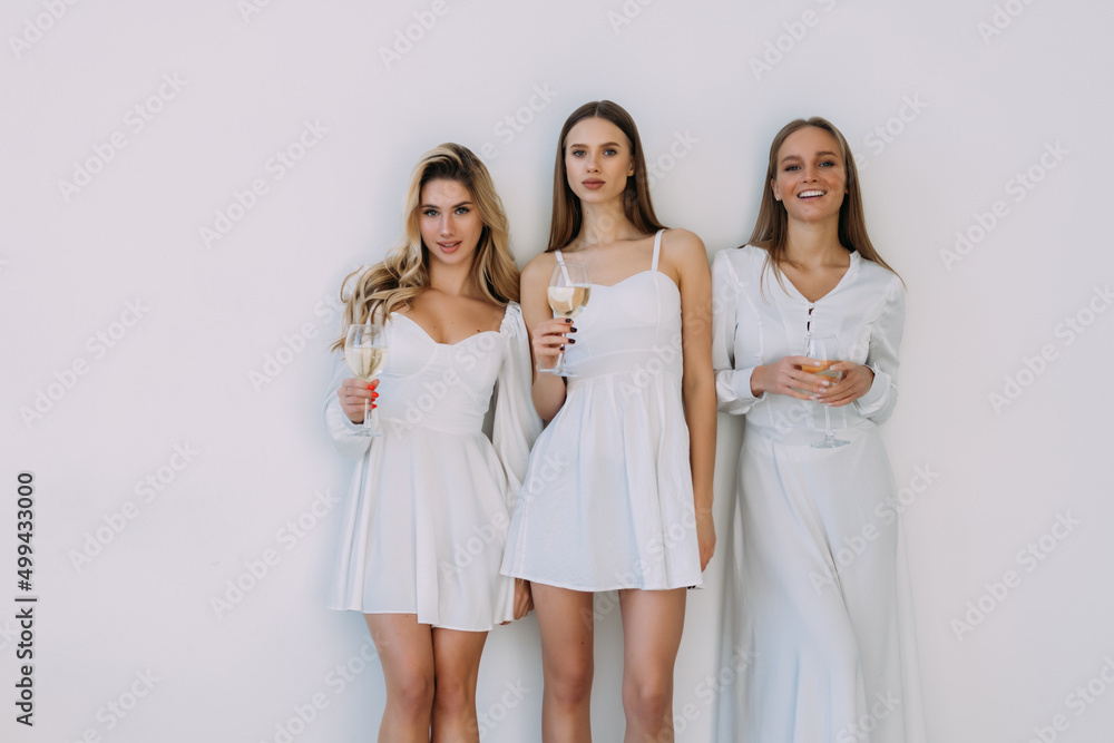 Three beautiful young smiling women celebrate in evening dresses of beige color, holding glasses with champagne. Three beautiful young smiling women celebrate in evening dresses of beige color, holding glasses with champagne.