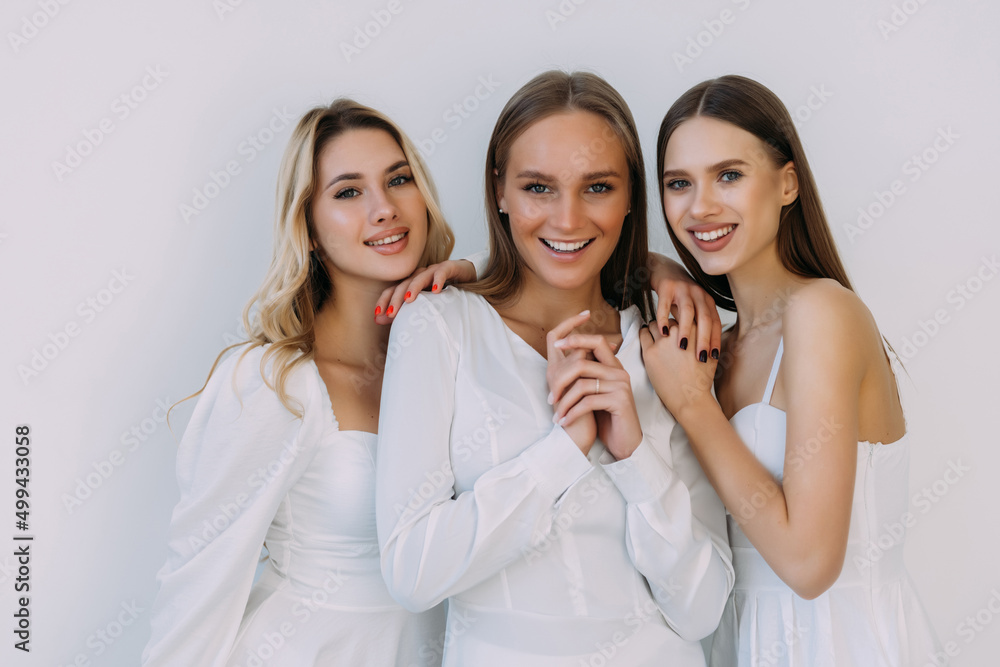 Three women smiling and looking at camera isolated over white wall Three women smiling and looking at camera isolated over white wall