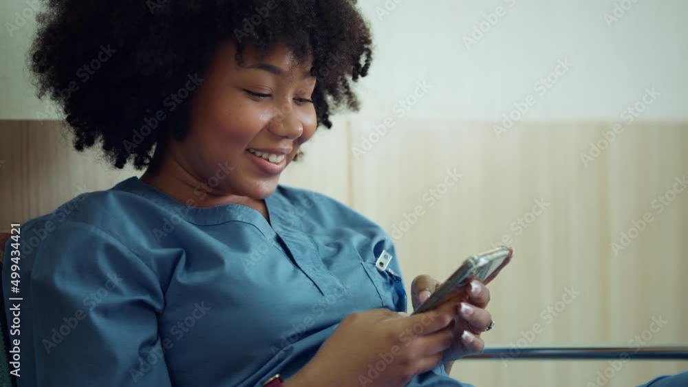 Happy African American female nurse dressed in scrubs using smartphone apps texting message to remote patient at hospital, Practice of medicine and public health care supported by mobile concept.